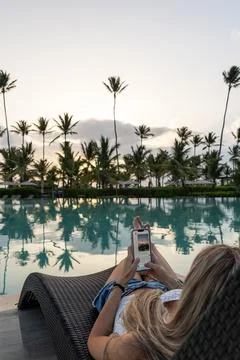 Tourist using smartphone by infinity pool at colombian resort during sunset Stock Photos