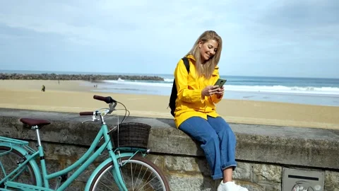 Tourist using smartphone while resting on beach wall with bicycle Stock Footage 304008823