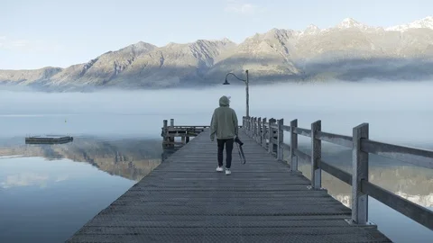 Tourist walking with camera towards end of jetty at fog covered Lake Wakatipu Stock Footage 119160403