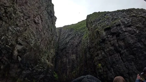 Tourists on a boat navigating a deep and narrow basalt sea gorge, Faroe Islands Stock Footage 339289136