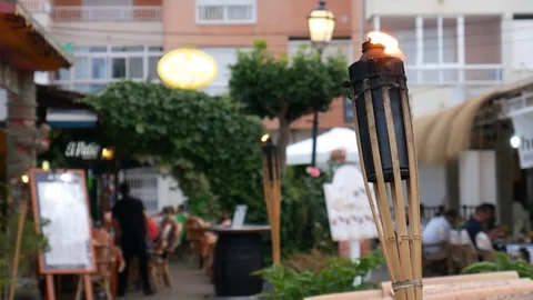 Tourists dining in a restaurant behind flame of torch in Playa de Muro Mallorca Video stock 81078231