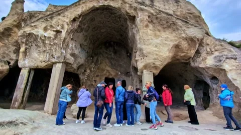 Tourists explore ancient rock carved halls at Uplistsikhe cave city Stock Footage 341060271