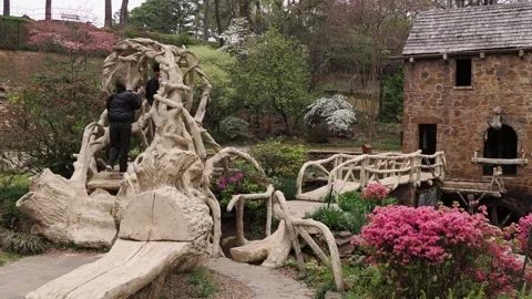 Tourists explore a rustic water mill in a lush spring garden. Stock Footage 345619428