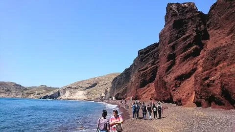 Tourists exploring the dramatic red volcanic cliffs of Red Beach in Santorini Stock Photos