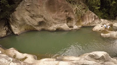Tourists exploring the rocks over a peaceful pool below Ba Ho waterfall. Stockbeeldmateriaal 74617353