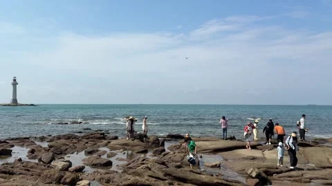 Tourists Exploring Rocky Coastline with Distant Ocean Lighthouse Video stock 330933075