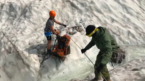 Tourists ferry a backpack through a turbulent stream in a glacier Stock-Footage 158670819