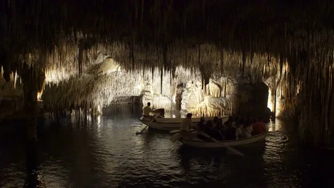 Tourists float on a boat on the underground lake in the famous stalactite caves Stock Footage