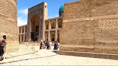 Tourists with a guide at Mir-i Arab Madrassah in ancient Bukhara Stock Footage 335539038