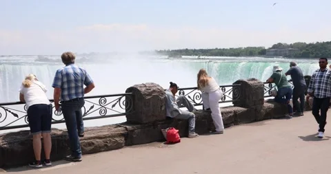 Tourists lean over Niagara Falls railing, mist rising from Horseshoe Falls. Stock Footage 321047950