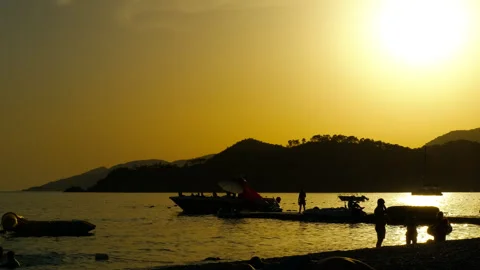 Tourists observing parasailing activity at sunset on beach Stock Footage 318035885