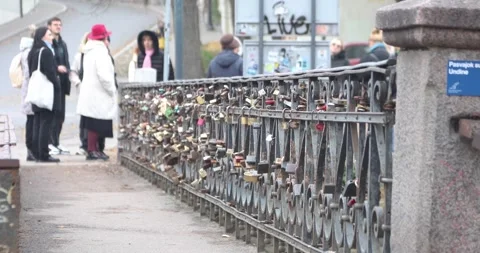 Tourists pass a bridge railing covered in love locks in Uzupis, Vilnius Stock Footage 321048345