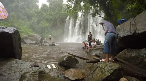 Tourists pose for pictures at base of a waterfall at Phnom Kulen National Par Видео 63575807
