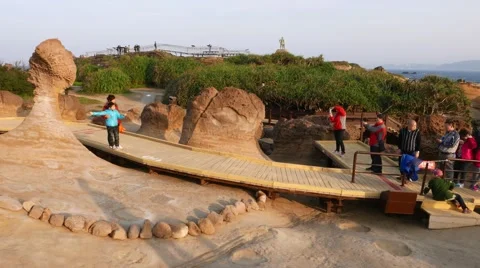 Tourists pose at Queen's Head Stone, famous eroded rock at Yehliu Geopark Stock Footage 57800857
