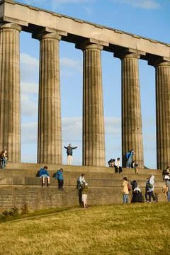 Tourists posing beneath towering classical columns at Edinburgh stone monument Stock Photos