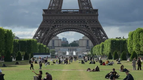 Tourists relax on Champ de Mars green lawn near the historic Eiffel Tower base Stock Footage 336725713