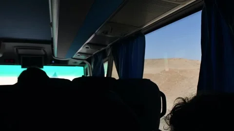 Tourists ride sightseeing bus through arid desert landscape, watching sunlit Stock Footage 337663692