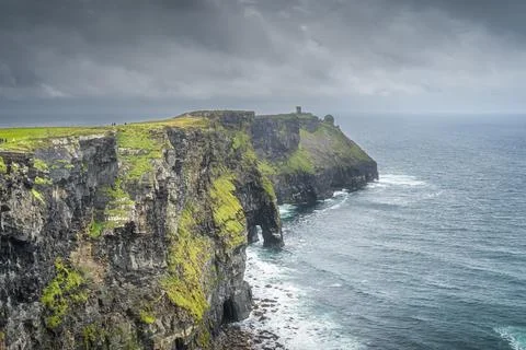 Tourists sightseeing Cliffs of Moher with Moher Tower on far distance, Ireland Stock Photos