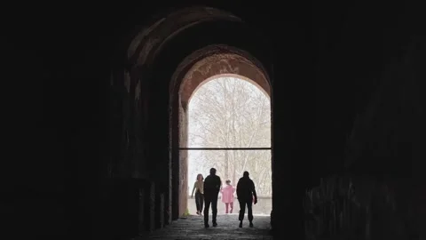 Tourists silhouetted inside a dark arched passage at Pompeii, walking toward 库存影片 336088178