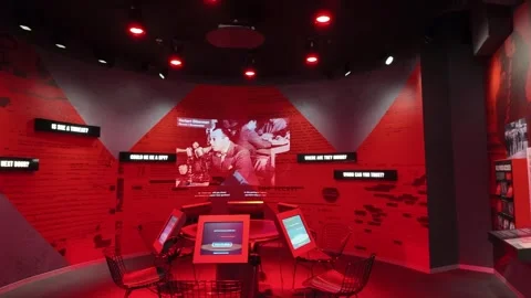 Tourists sit at interactive screens in a red dimly lit spy museum exhibit. Video stock 333920906