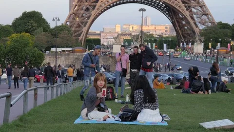 Tourists sit rest on green lawn by the Eiffel Tour in Paris taking selfie Stock Footage 76350341