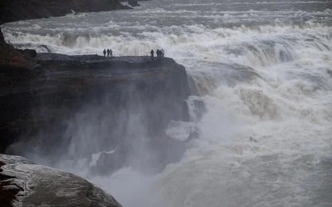 Tourists standing on a cliff at gullfoss, experiencing the immense power of t Stock Photos