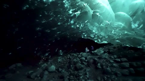 Tourists use flashlights to explore a frozen blue glacial water ice cave in Stock Footage 312093673