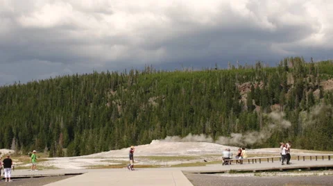 Tourists walk about the boardwalk as the Old Faithful geyser steams behind them Stock Footage 46419772
