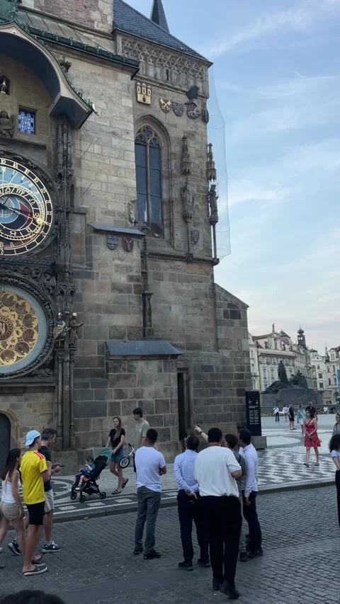 Tourists walking and pausing in historic plaza before ornate astronomical clock Stock Footage 344585297