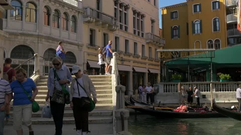 Tourists walking on a bridge while a man is paddling a gondola in Venice Stock Footage 57398834