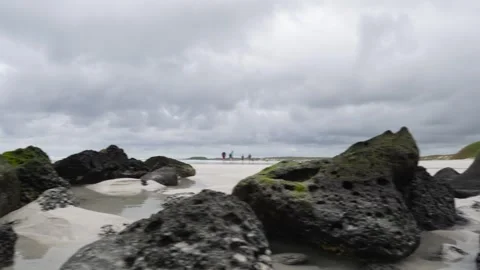 Tourists walking on a cloudy beach with black rocks 스톡 동영상 310190830