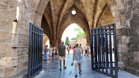 Tourists walking through open iron gate and medieval arch in Rhodes Stock Footage 340575855