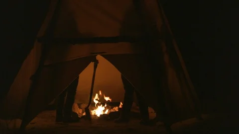 Tourists warming themselves around the campfire in tent at night Stock Footage 101200893