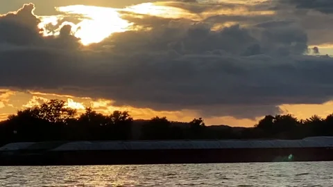 A tow boat pushing multiple barges plies the Mississippi River at sunset Stock Footage 146095629