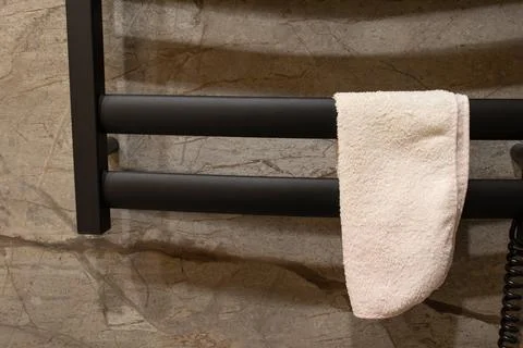 A towel is draped on a black heating rack in a bathroom. The wall has a sto.. Stock Photos