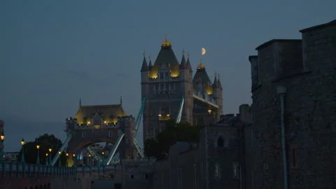 Tower Bridge illuminated at dusk with a half moon above and castle walls nearby. Video stock 321607388