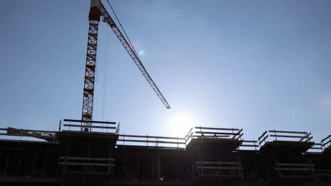 Tower crane and skeletal frame of a building silhouetted against the bright sun. Stock Footage 306007897