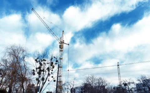Tower crane by blue cloudy sky and branch of trees Stock Photos
