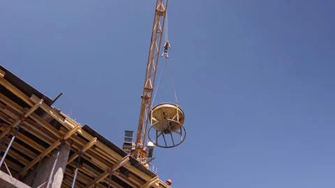 Tower crane lifting concrete bucket above building construction site low angle 스톡 동영상 341986201