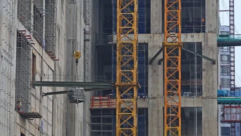 Tower crane lifting heavy building materials up the side of concrete high-rise Stock Footage 337989522