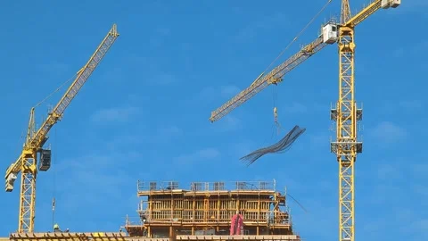 A tower crane lifts rebar at a construction site with workers on scaffolding Vídeos de archivo 301872948
