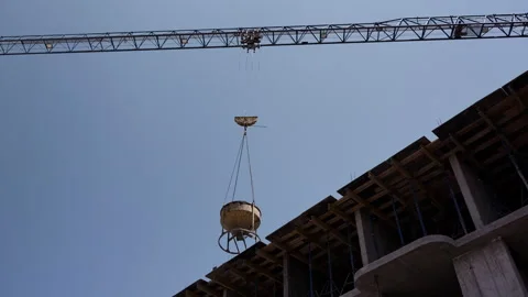 Tower crane lowering concrete bucket onto unfinished building wide shot Stock Footage 341986105