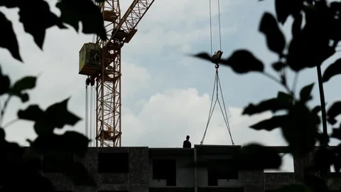 Tower crane lowering prefabricated concrete slab to builder working at height on Stock Footage 346639457
