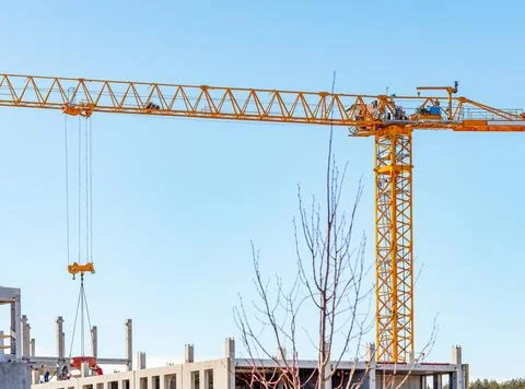 Tower crane operating at a modern construction site under blue sky. Yellow .. 库存照片