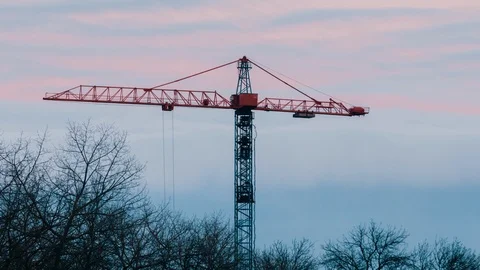 Tower crane working on construction site trees with no leaves trembling in wind Stock Footage 103996253