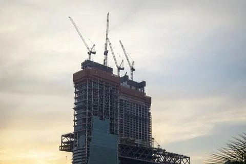 Tower cranes in action at construction site on sunset background. Crane the b Stock Photos