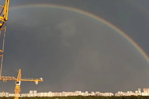 Tower cranes against sky with clouds and rainbow. Stock Photos