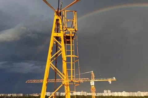Tower cranes against sky with clouds and rainbow. Stock Photos