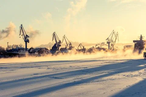 Tower cranes in white winter background, shadows on frozen river Stock Photos