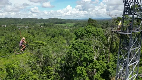 Tower in middle of green forest, to which cyclist rides on steel rope. An aerial Stock Footage 231588675